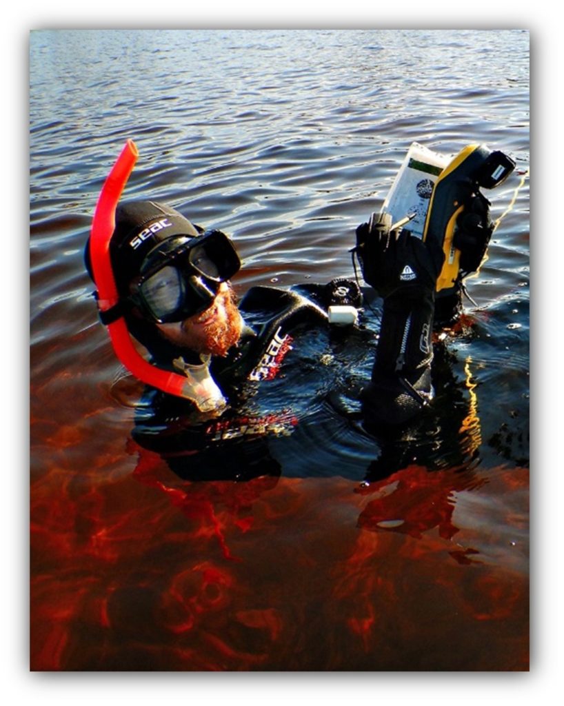 Person in a snorkel mask floating in the water holding a device out of the water.